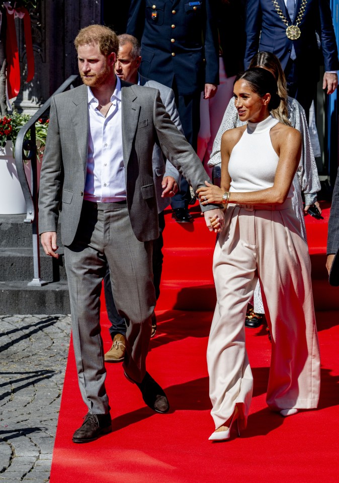 prince harry and meghan markle walk on a red carpet