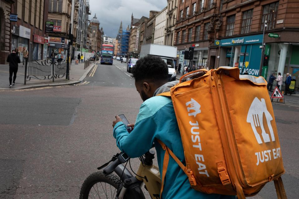 a man riding a bike with an orange just eat bag on his back