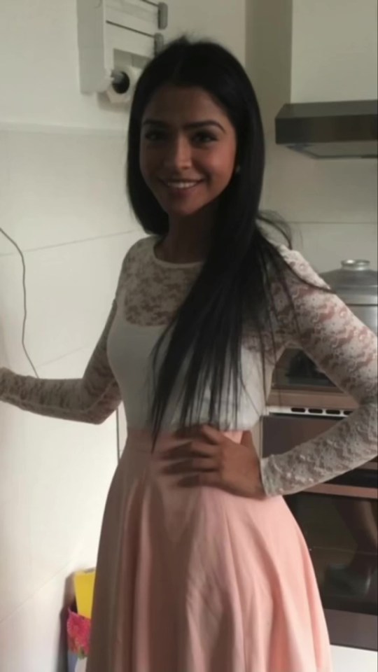 a woman wearing a white top and a pink skirt smiles for the camera