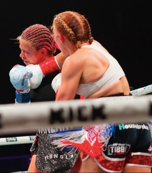 two female boxers are fighting in a ring sponsored by kick