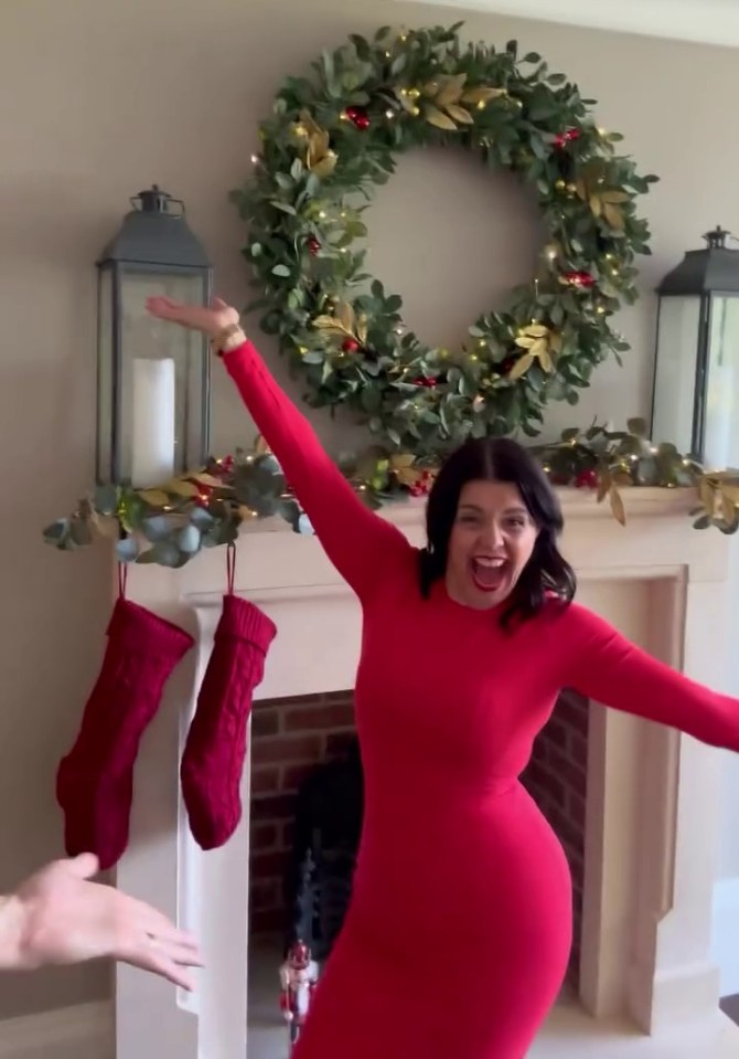 a woman in a red dress is standing in front of a christmas wreath