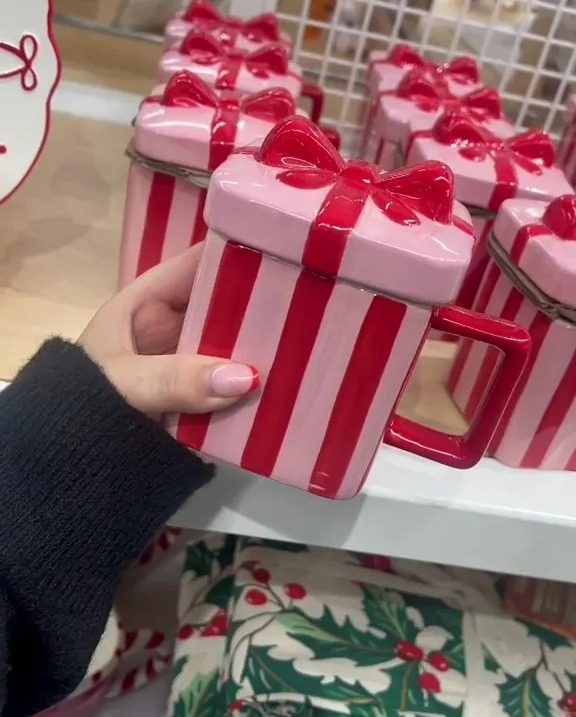 a person is holding a pink and red striped mug with a red bow