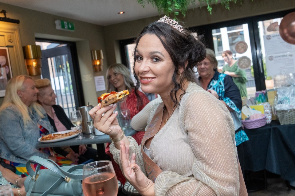 a woman wearing a tiara holds a glass of wine and a slice of pizza