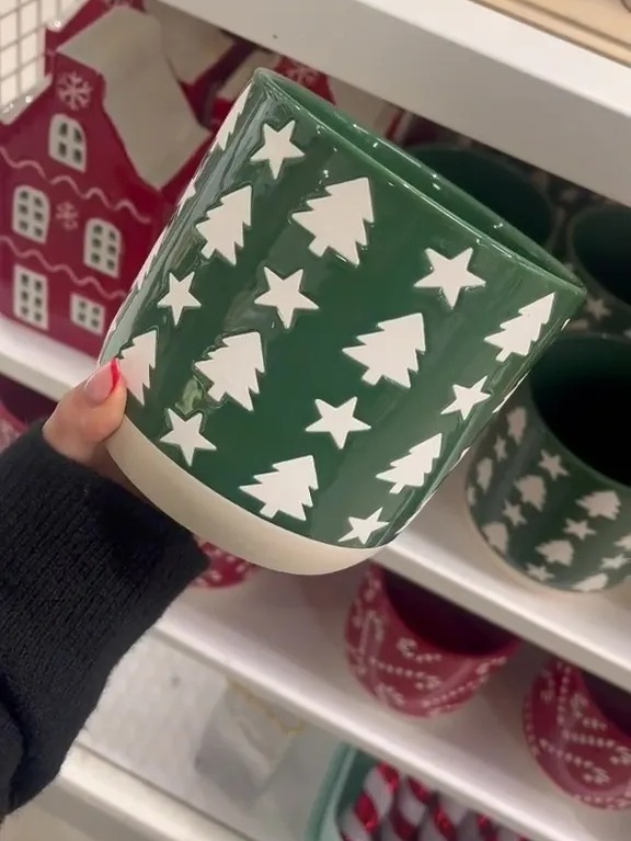 a person is holding a green pot with white trees and stars on it