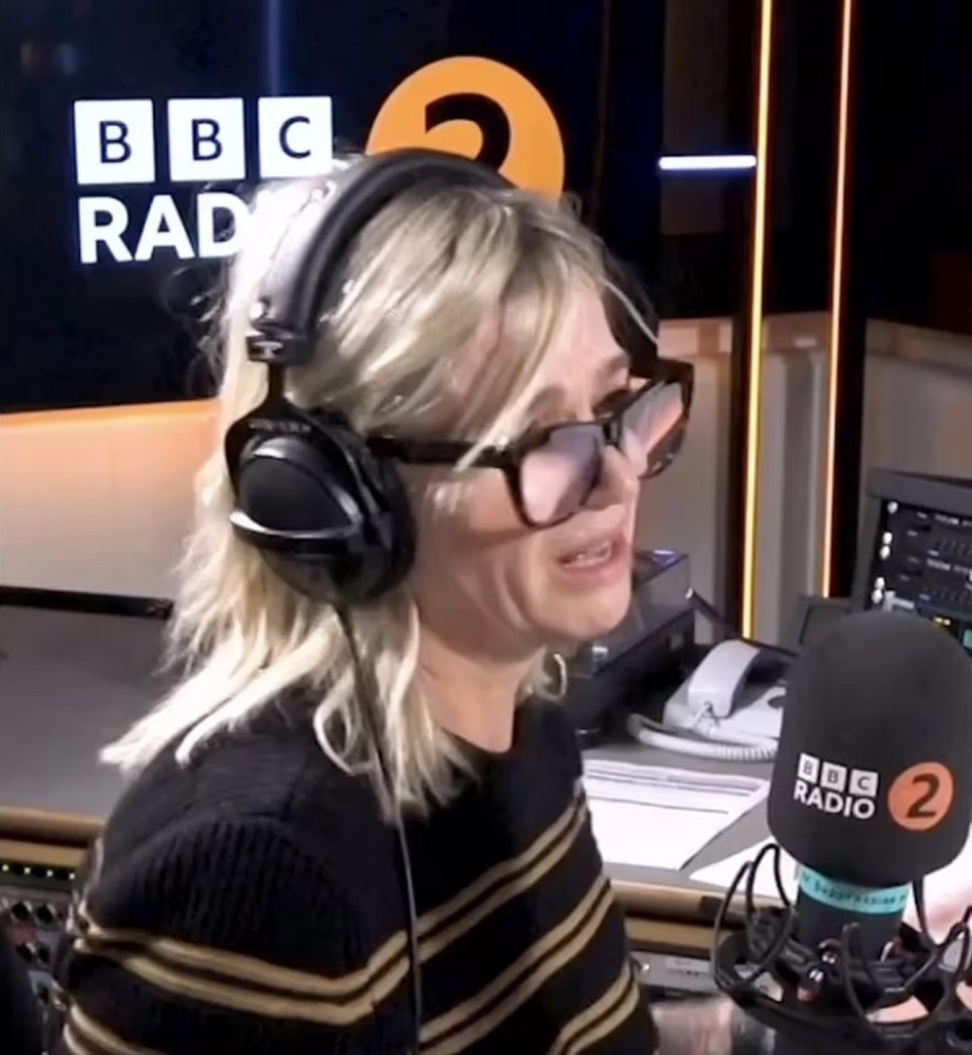 a woman wearing headphones stands in front of a bbc radio 2 microphone