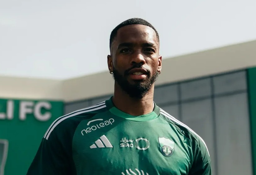 a man holding a soccer ball in front of a building that says al ahli fc