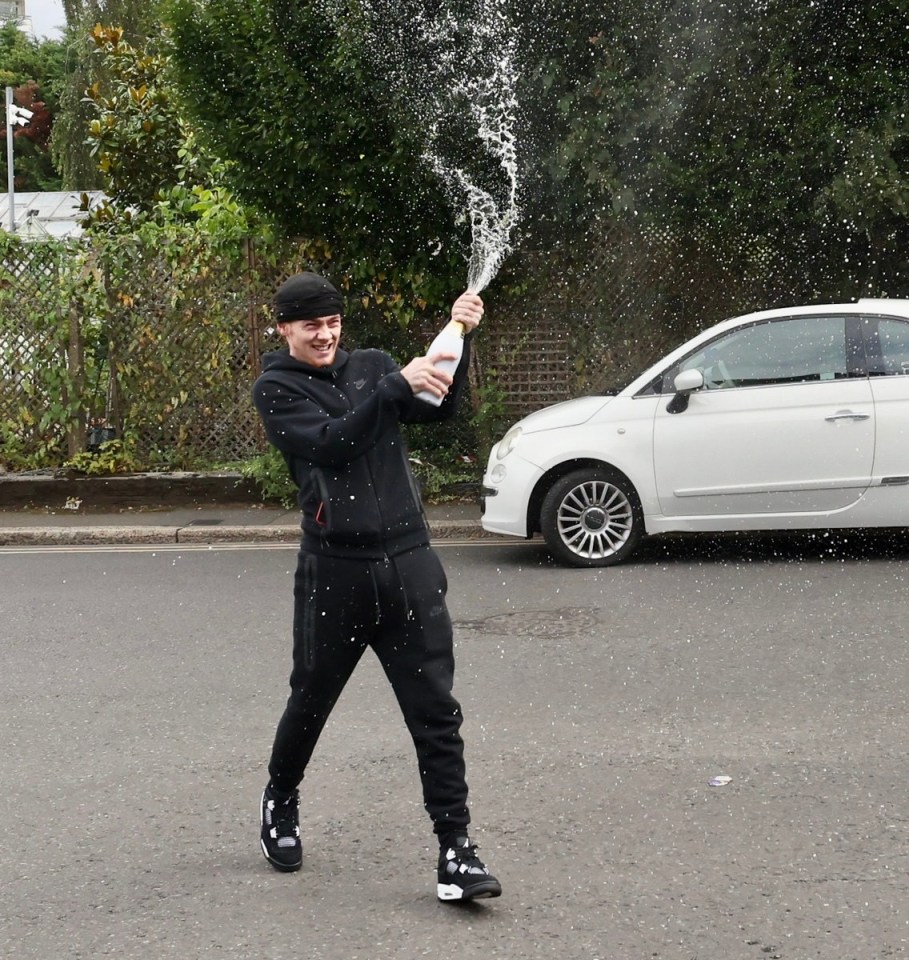 a man is holding a bottle of champagne in front of a white car