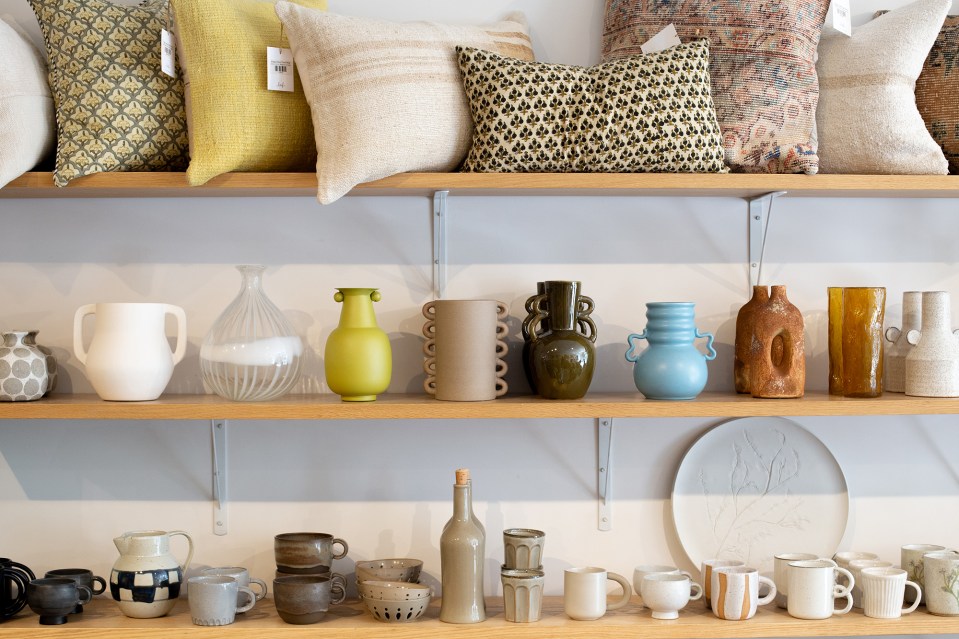 a shelf full of vases and mugs with a yellow pillow on top