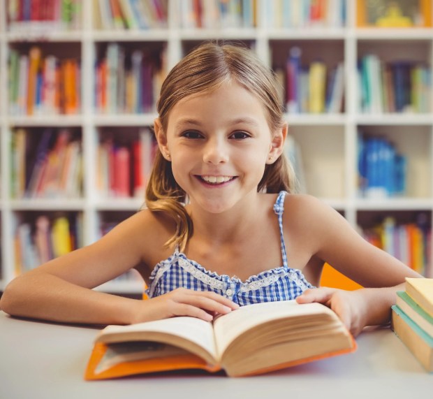 a little girl sits at a table reading a book