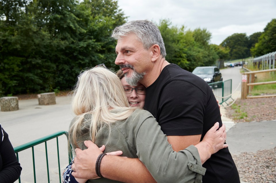 a man in a black shirt is hugging a woman in a green jacket