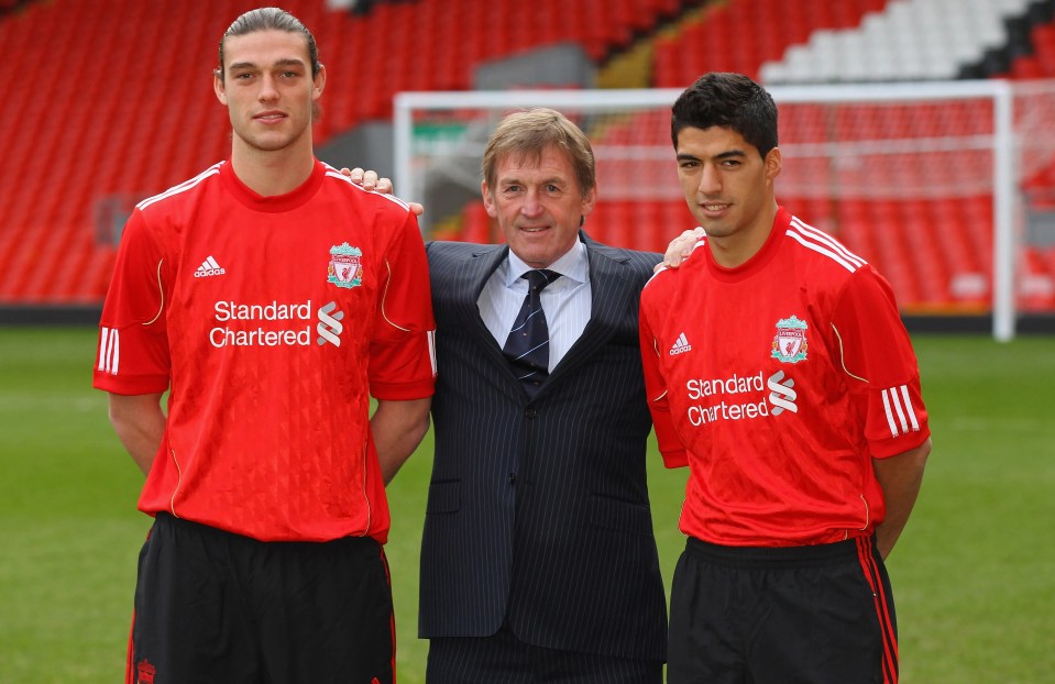 a man in a suit stands between two soccer players wearing red jerseys that say standard chartered