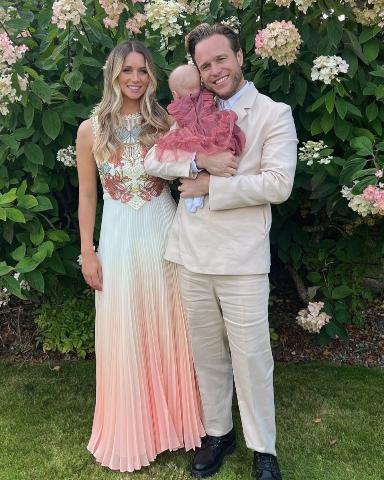 a man and woman holding a baby in front of flowers