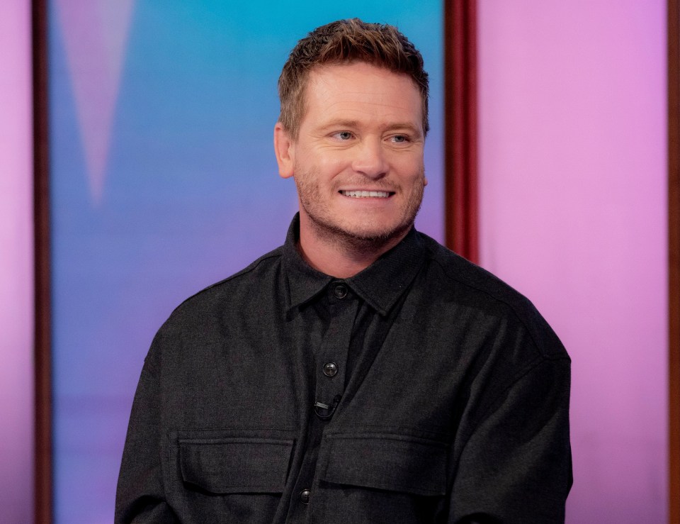 a man in a black shirt is smiling in front of a pink background