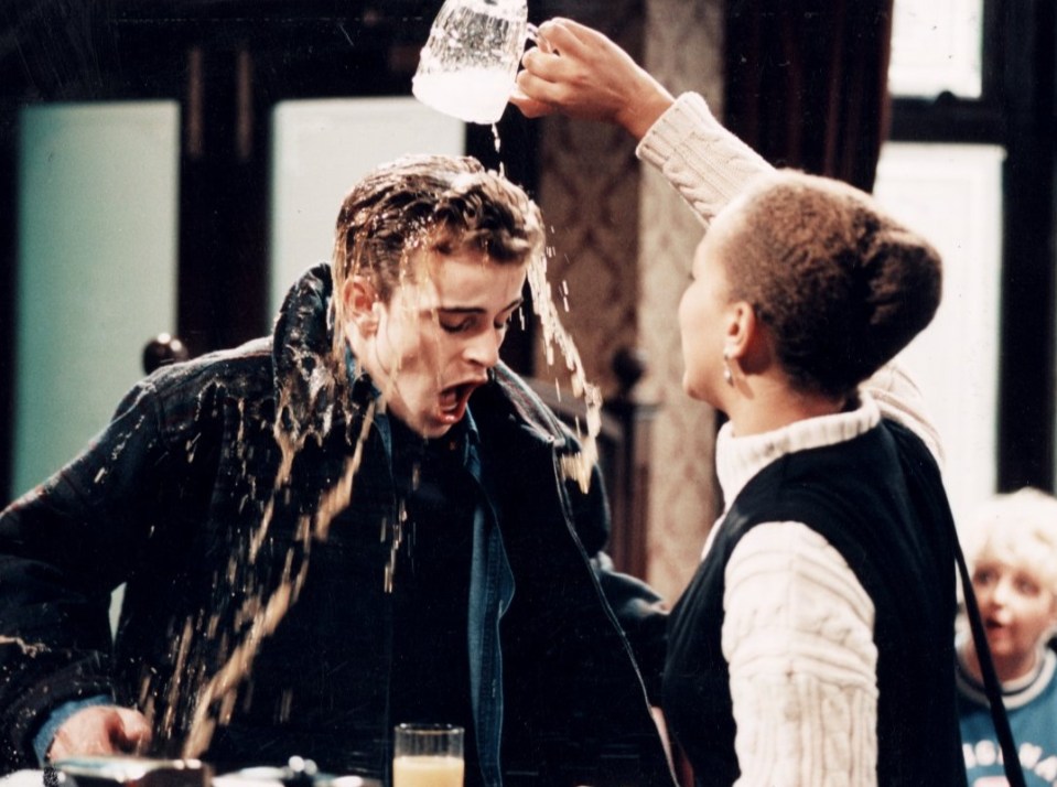 a woman pours a glass of orange juice on a man 's head