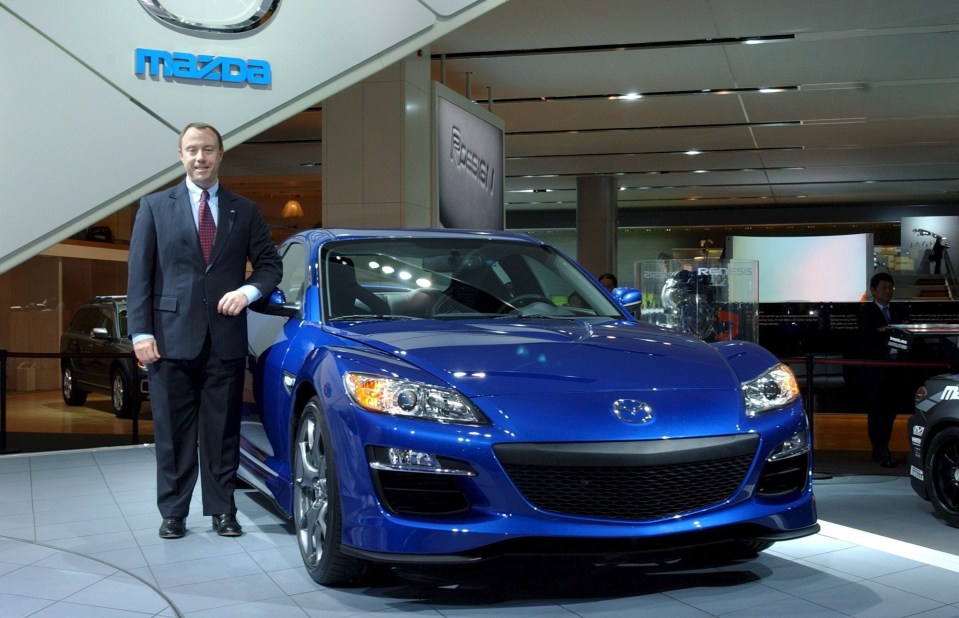 a man stands in front of a blue mazda car