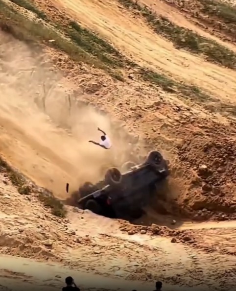 a man in a white shirt is falling off a vehicle in the dirt