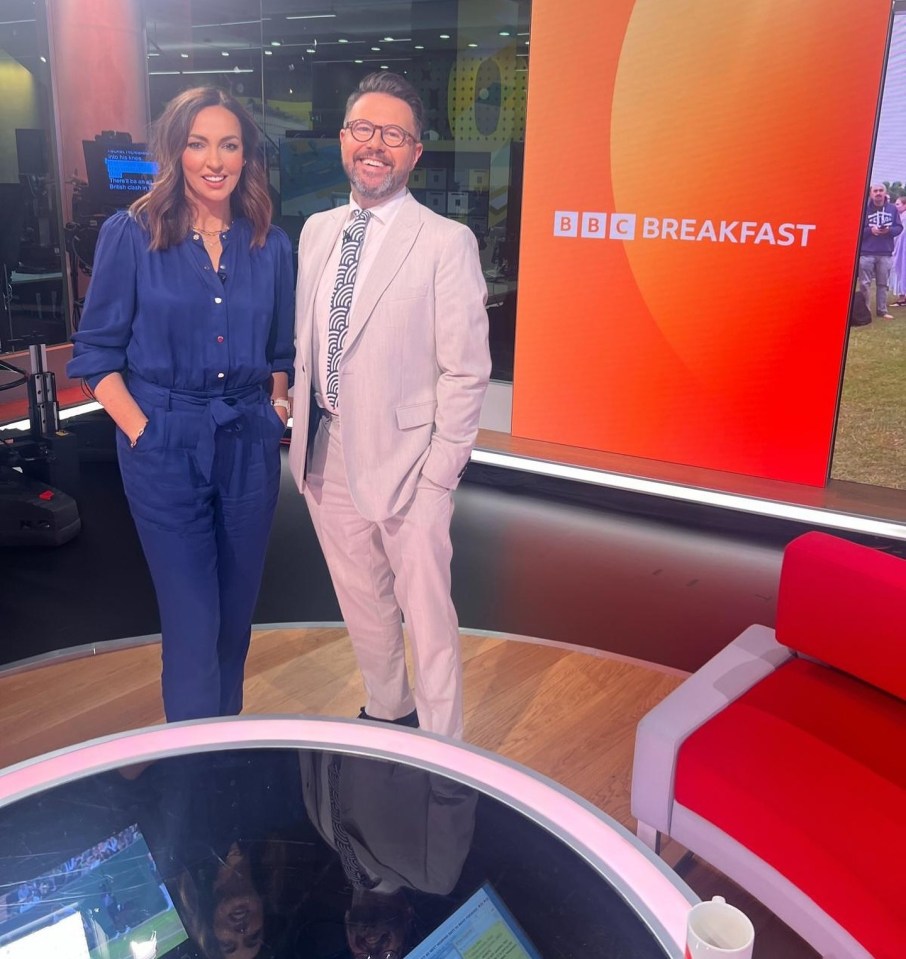 two people standing in front of a bbc breakfast sign