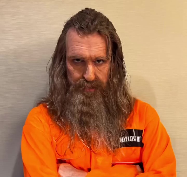 a man with long hair and a beard is wearing an orange jumpsuit