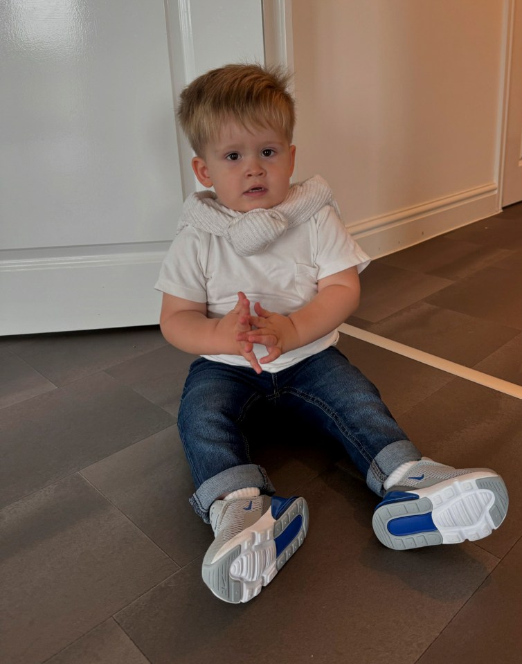 a little boy wearing nike shoes sits on the floor