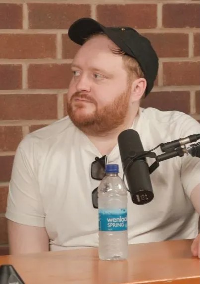 a man with a beard is sitting in front of a microphone and a bottle of wendalo spring water