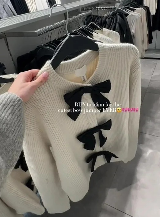 a person is holding a white sweater with black bows in a store