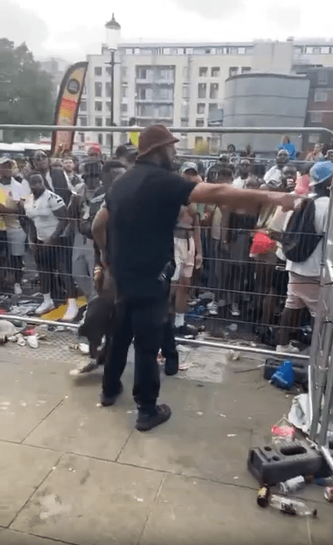 a man in a hat is pointing at a crowd of people behind a fence .