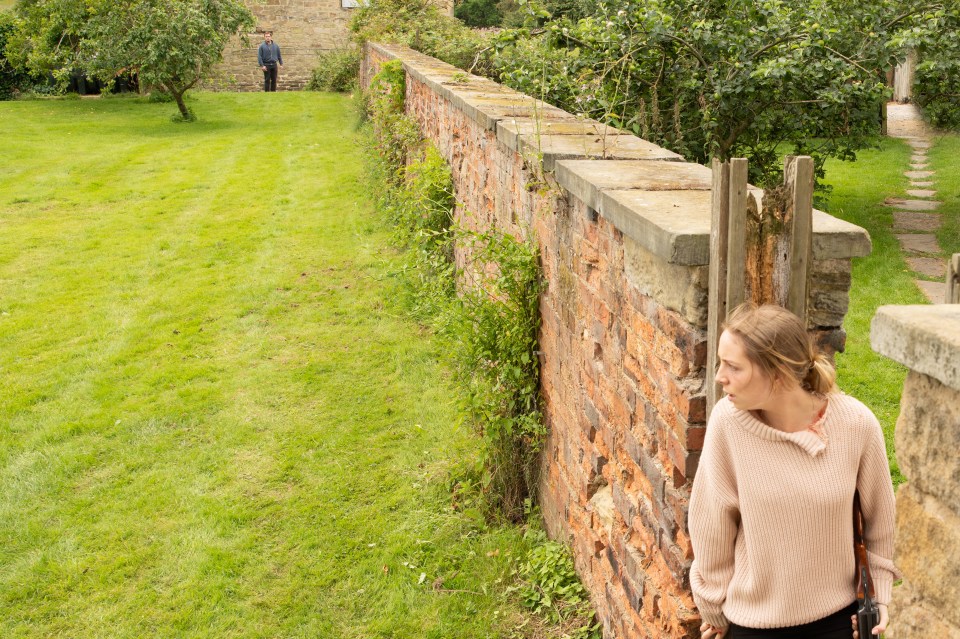 a woman in a pink sweater leans against a brick wall