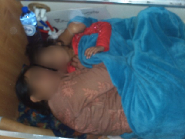 a woman and child are laying under a blue blanket