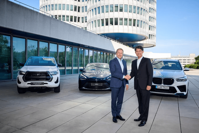 two men shaking hands in front of a bmw x5 and a toyota hilux