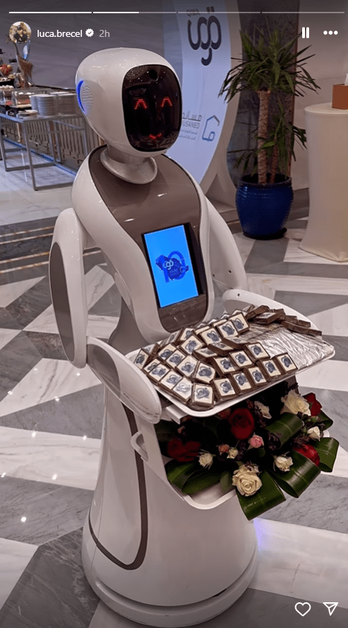 a robot is holding a tray of chocolates in front of a sign that says luca brecel