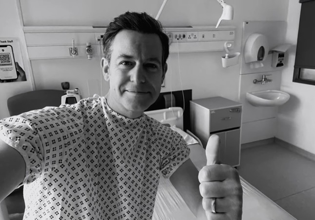 a man in a hospital gown gives a thumbs up