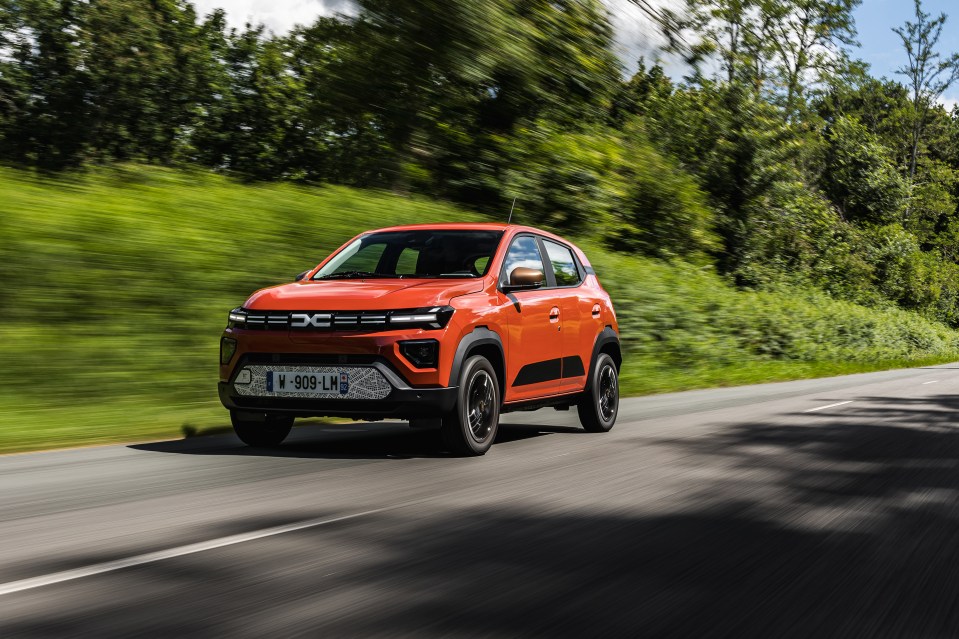 an orange dacia car is driving down a road