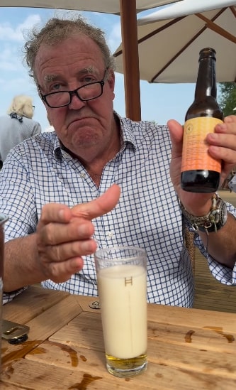 a man is holding a bottle of beer and a glass with the letter h on it