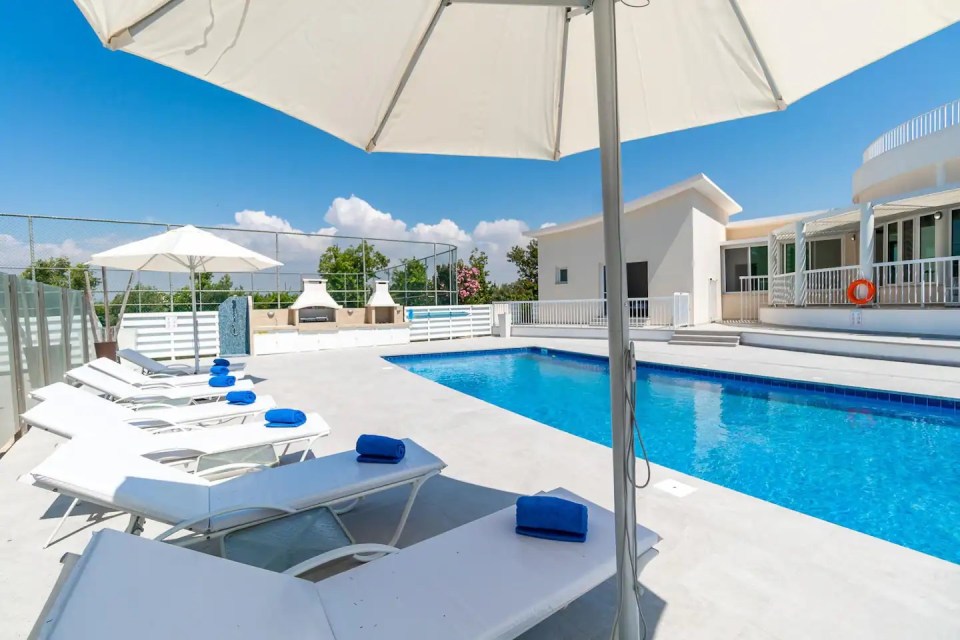 a large swimming pool with white chairs and umbrellas