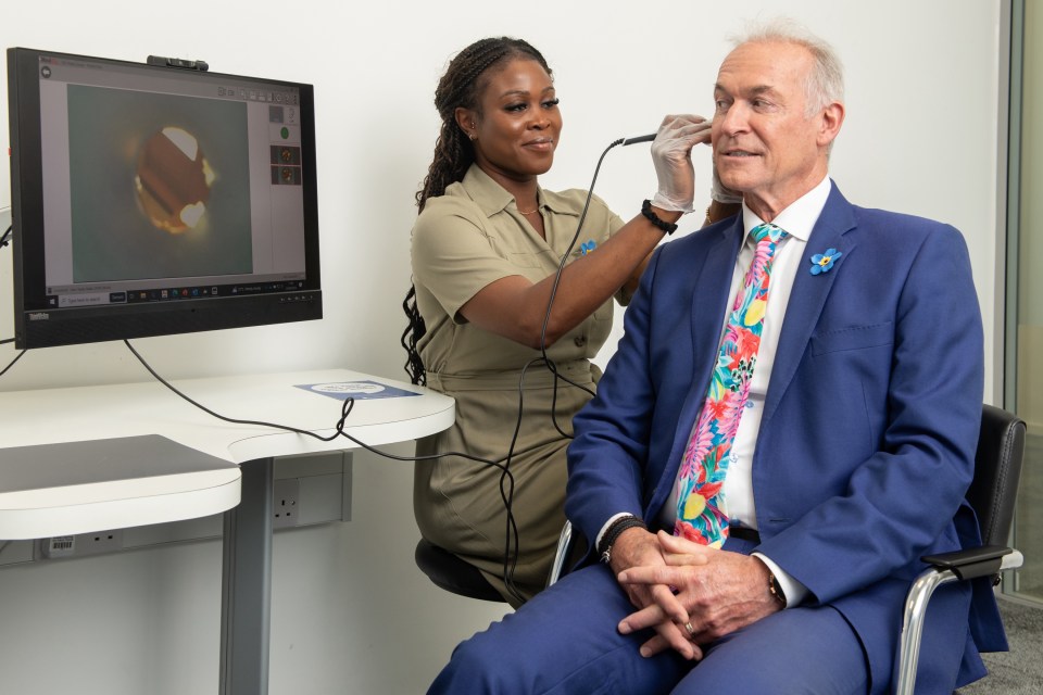 a woman examines a man 's ear in front of a dell monitor