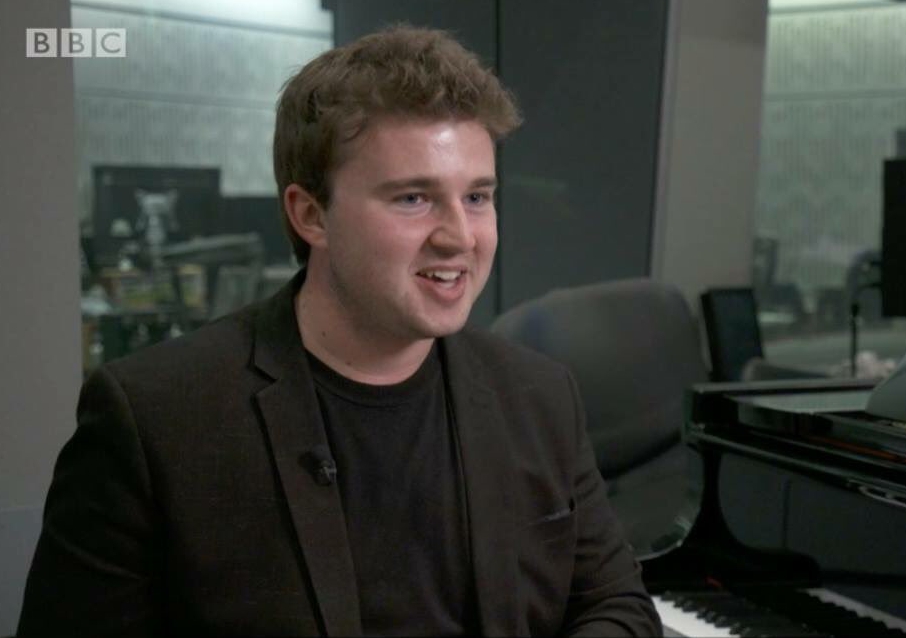 a man sitting in front of a piano with bbc written on the bottom