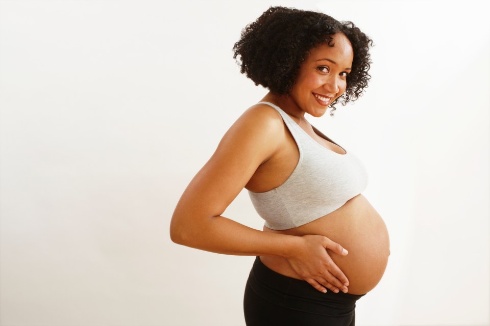 a smiling pregnant woman holds her hand on her belly