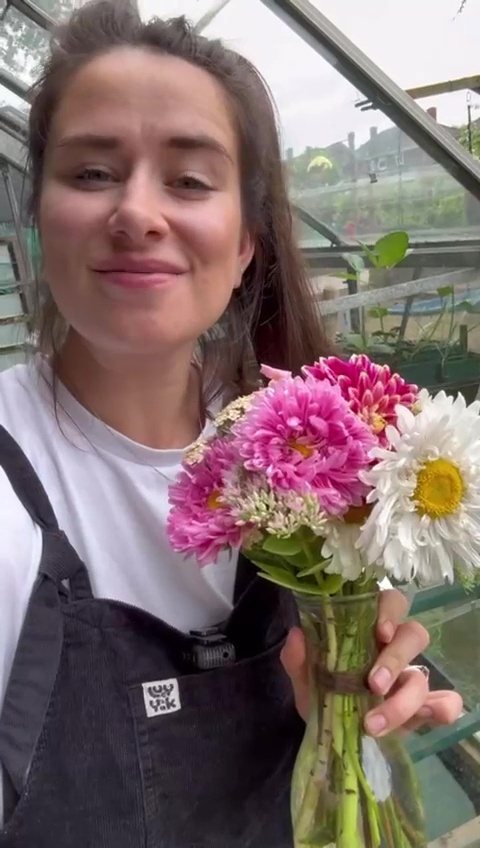 a woman is holding a vase of flowers in a greenhouse .