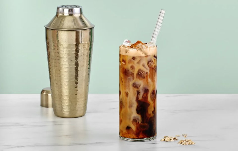 a tall glass of iced coffee next to a shaker