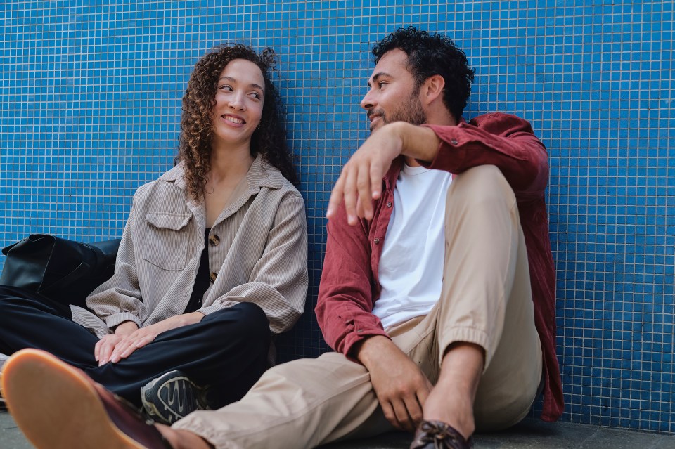 a man and a woman sit next to each other in front of a blue tiled wall