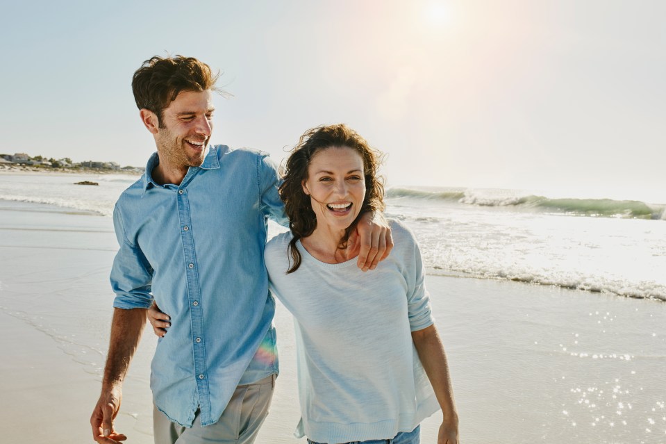 a man and woman are walking on the beach and the woman is smiling