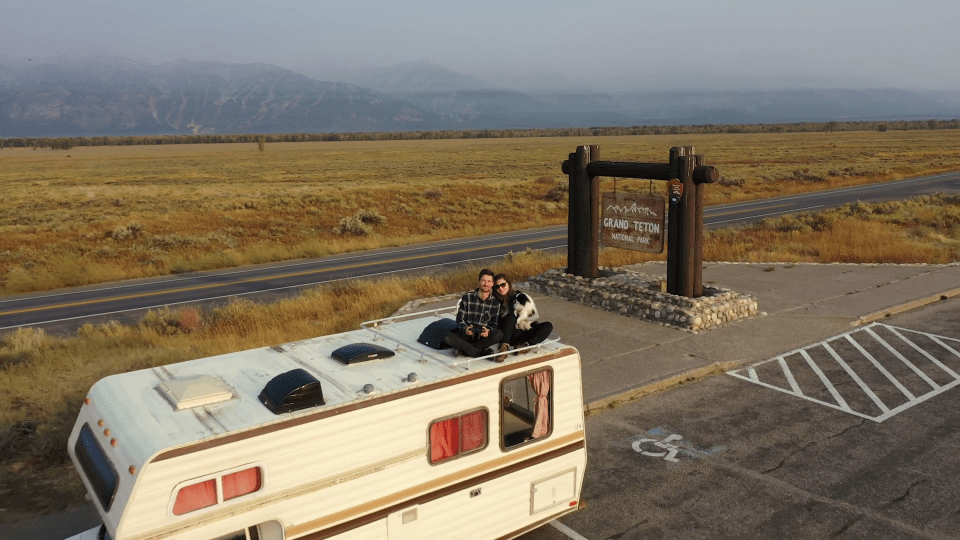 a couple sitting on top of a rv in front of a sign that says grand teton national park