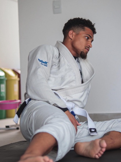 a man in a white hawk martial arts uniform sits on a mat