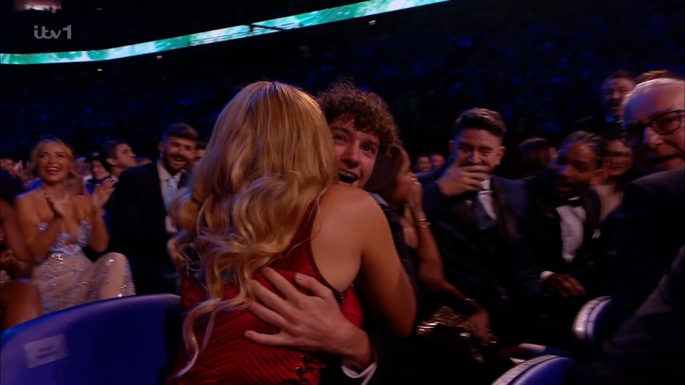 a woman in a red dress is hugging a man in front of a tv screen that says itv 1