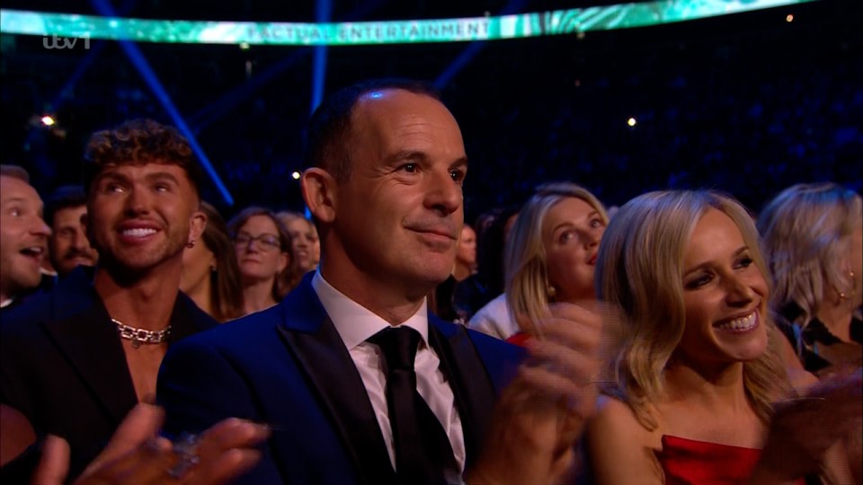 a man in a suit and tie applauds in front of a sign that says global entertainment