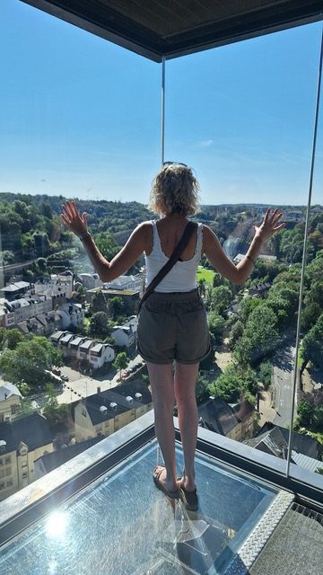 a woman is standing on a glass floor looking out over a city .