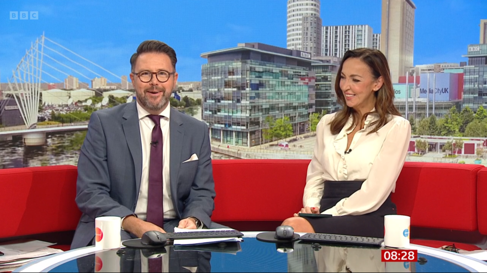 a man and a woman sit in front of a bbc sign