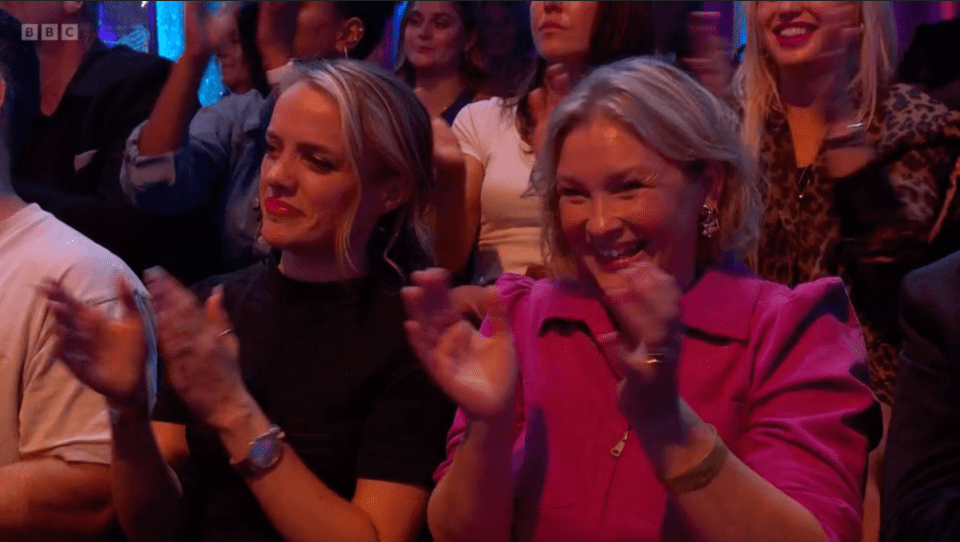 a woman in a pink shirt applauds while sitting in a bbc audience