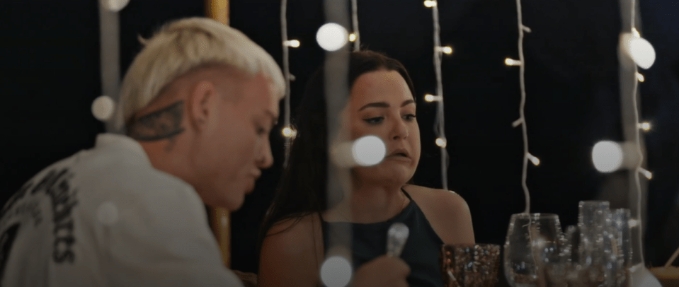 a man and a woman sit at a table with a string of lights behind them