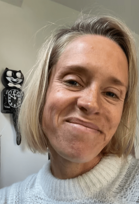 a woman making a funny face in front of a black cat clock